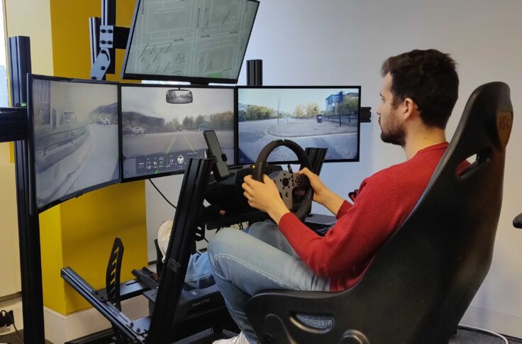 Man sitting in front of screens with a steering wheel in his hands