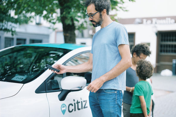 man standing next to a citz car and using a smartphone to rent it