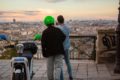 two men standing next to a cooltra moped and enjoying a view over a city from behind. one is wearing a green cooltra helmet