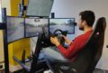 Man sitting in front of screens with a steering wheel in his hands