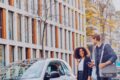 A woman and a man accesses a shared vehicle parked curbside at the university.